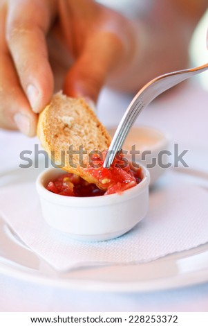 A picture of a red sauce in a small pot and a hand soping white bread into the sauce.