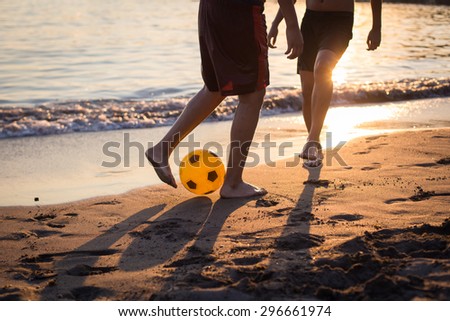 Two guys playing football on the beach at sunset legs closeup