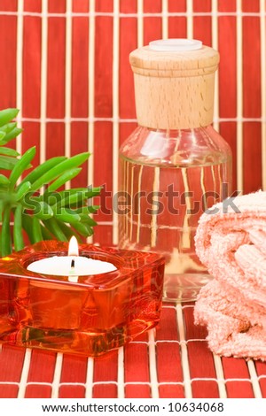 Aromatherapy bottle with towel, candle and green plant on bamboo