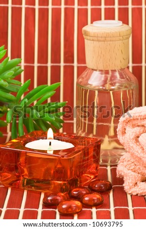 Spa scene with towel, aromatherapy bottle, glass pebbles, candle and green plant on colored bamboo