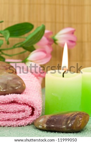 Spa stones with candles, towel with decoration flowers on bamboo background, focus on front stone