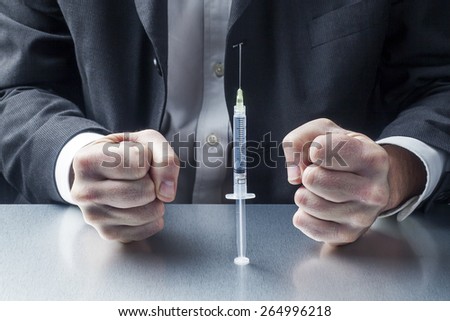 male business fists facing a syringe on his desk