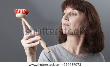 beautiful mature woman contemplating dish brush as an obsessive cleaning housewife