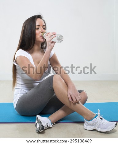 thirsty young fitness woman sitting on an exercise mat with gym clothes drinking water for hydration after pilates class