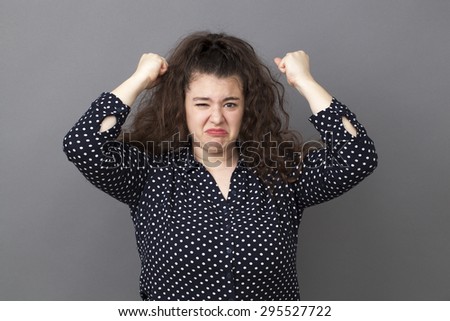 angry overweight 20\'s woman expressing exasperation and frustration with both fists up and funny face