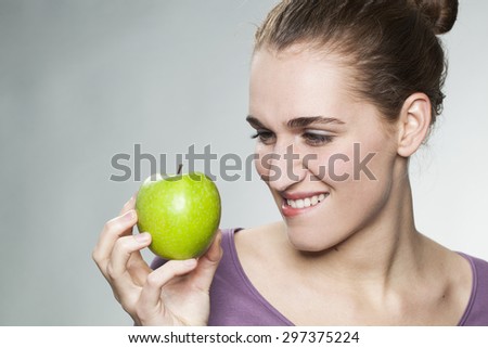happy beautiful young woman biting lips to resist in eating appetizing green apple for symbol of beauty and healthy nutrition