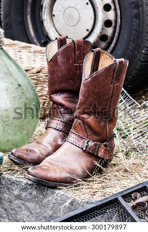 old leather cowboy boots on sale at garage sale for collection, welfare or selling for cheap to cope with over-consumption and fashion