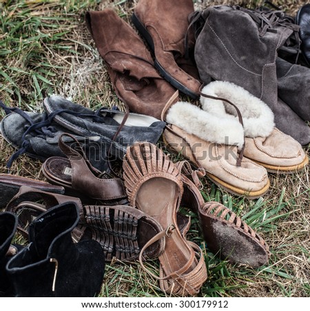 mix of used leather women boots and shoes on sale at garage sale on grass for donation, recycling or selling for cheap to cope with over-consumption and fashion