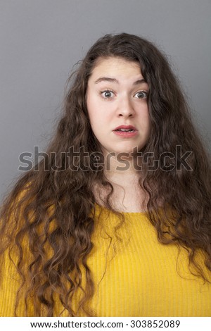 fear concept - young xxl woman with long brown hair looking surprised and scared, studio shot