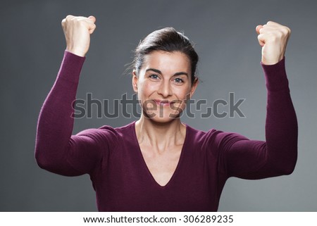 success concept - happy young woman with both hands up holding her fists up for winning competition with serenity,using body language