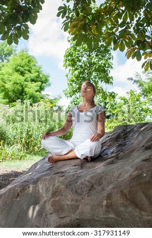outdoors zen exercise - focused young yoga woman escaping in closing eyes,relaxing bare feet on a big stone, summer daylight.