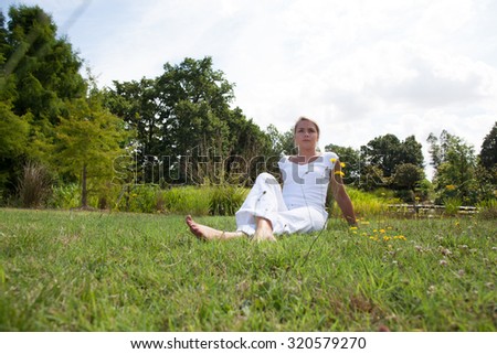 relaxation outside - relaxed young woman with bare feet sitting on grass with trees and park surroundings, summer daylight and blue sky, low angle view