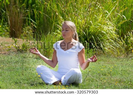 outdoors meditation - young yoga woman breathing in lotus pose,closing eyes to focus on inner peace to relax and meditate on grass with green bushy background
