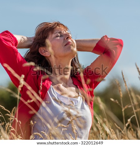 female casual relaxation - thinking beautiful mature woman looking up, breathing in harmony with nature in long dry summer meadow seeking for peace,summer daylight