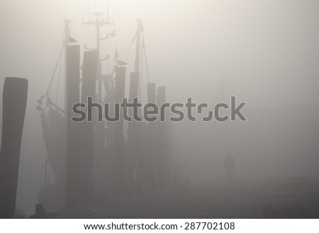 Man Walking Past Masted Ship in Harbor at Dock Obscured by Thick Blanket of Fog in Dorum, Germany