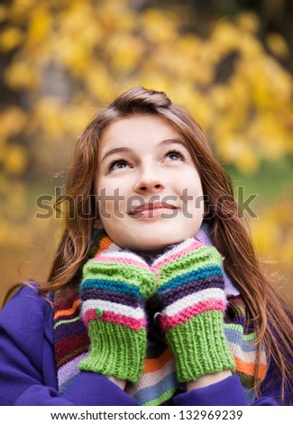 Portrait of an attractive young woman with hands in mittens near face in the autumn park