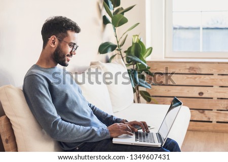 Photo of Handsome young man using laptop computer at home. Student men resting  in his room. Online shopping, home work, freelance, online learning, studying concept. Distance education