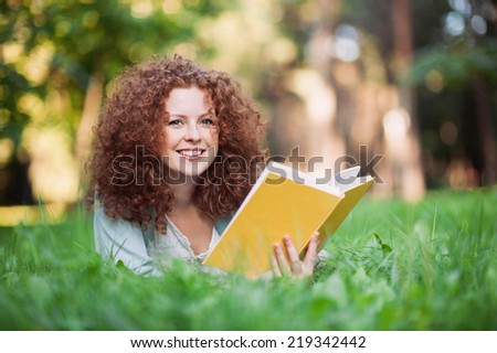Beautiful girl holding an open book, summer green park background.
