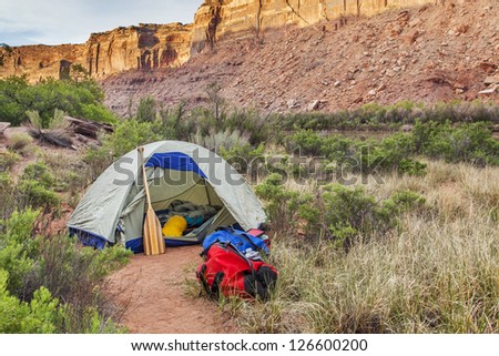 sunrise over river camping in Canyonlands National Park- a tent with canoe paddle and waterproof bags on the shore of Green River