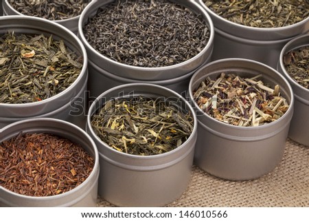 samples of loose leaf green, red, black and herbal tea in metal cans on canvas background