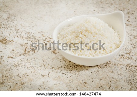 small ceramic bowl of  coconut flakes against a ceramic tile background with a copy space