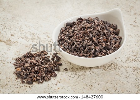 small ceramic bowl of  raw cacao nibs  against a ceramic tile background with a copy space
