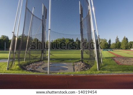 green grass athletic field with a hammer throw cage and long jump sand pit, early morning light