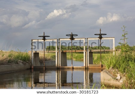 irrigation ditch with flowing water in northern Colorado, three gates, lifting gear and foot bridge