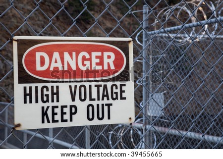 danger, high voltage, keep out -  warning sign on a chain link fence with barbed wire on top protecting hydro power plant