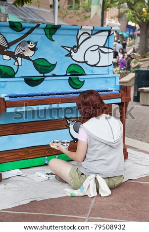 FORT COLLINS, COLORADO, USA - JUNE 18, 2011: Artist Ren Burke paints a mural on the piano in Fort Collins Old Town Square as part of Pianos About Town public art program. June 18, 2011.