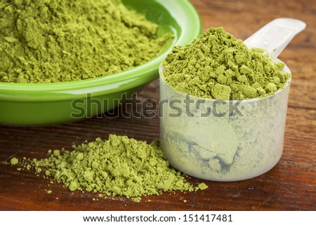 measuring scoop of moringa leaf powder with a bowl on wooden surface
