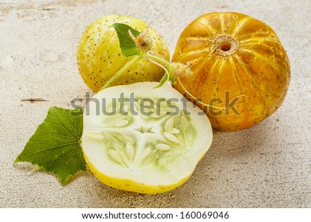 lemon (or apple) cucumbers with cross section and leaf on rough white painted wood surface