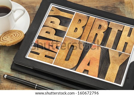Happy birthday in letterpress wood type on digital tablet computer with stylus pen, coffee cup and cookie