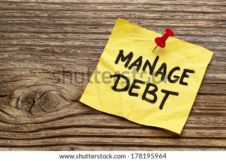 manage debt - yellow reminder note against grained wood board