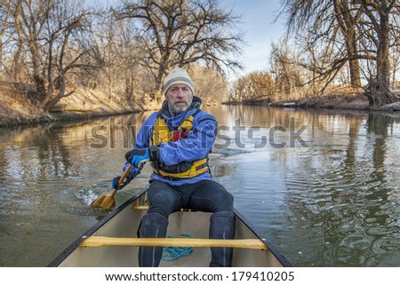 senior canoe paddler in a  canoe on the Cache la Poudre River, Fort Collins, Colorado, winter or early spring, view from the bow
