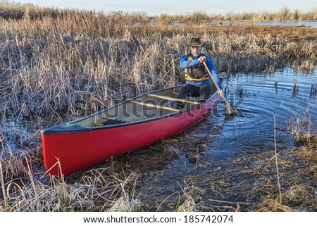 senior male paddling a red canoe through a wetland in early spring