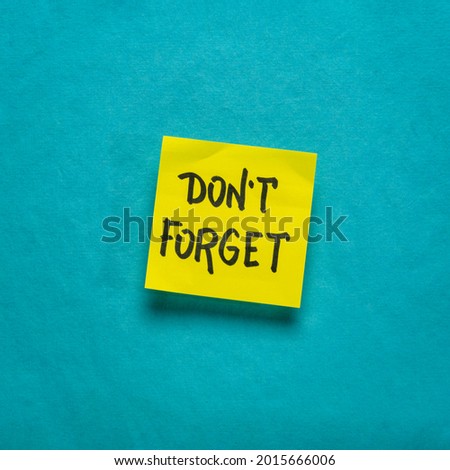 do not forget reminder - handwriting on a yellow sticky note against blue handmade paper