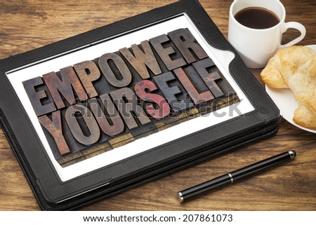 empower yourself - motivation concept - text in vintage letterpress wood type blocks stained by ink on a digital tablet with cup of coffee