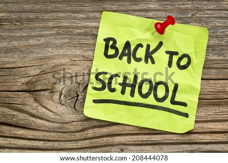 back to school reminder - handwriting on a green sticky note against grained anf knotted wood board