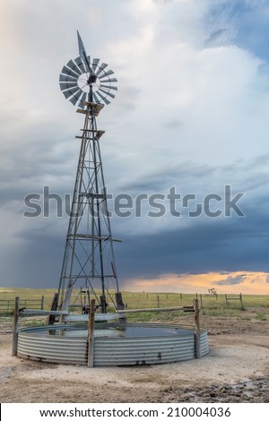 windmill with a pump and cattle water tank in shortgrass prairie against stormy sky, iPawnee National Grassland in Colorado near Grover