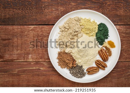 dry ingredients of healthy breakfast smoothie: whey protein, cacao, chia seeds, pecan nuts, maca root powder, spirulina,  spices (cinnamon, ginger, turmeric) on a rustic wooden table