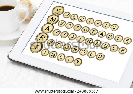 SMART goal setting acronym (specific, measurable,attainable,recorder, timely)  in old round typewriter keys on a digital tablet with cup of coffee