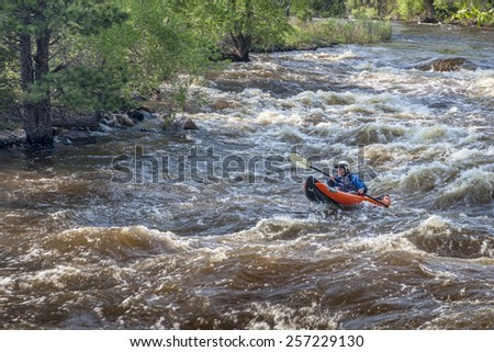 FORT COLLINS, CO, USA - JUNE 4, 2011: Female kayaker paddling inflatable boat over Maddog Rapid on Cache la Poudre River west of Fort Collins, Colorado as snow pack in the high country begins to melt.