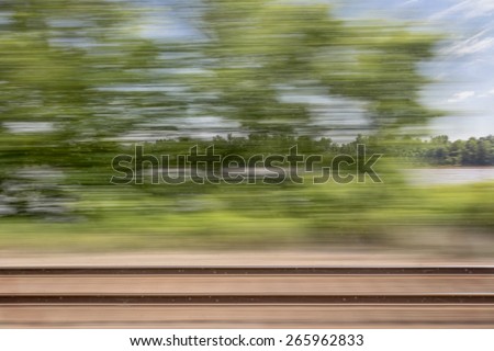 blurry abstract landscape of rail tracks and a river seen from train window in motion