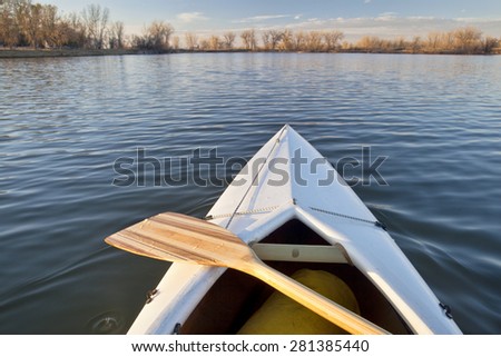 bow of white canoe with wooden paddle on a calm lake in Colorado