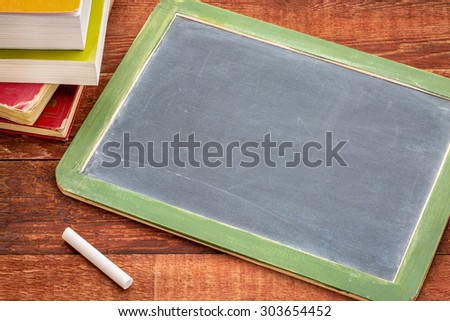blank slate blackboard with a white chalk and a stack of books against rustic wooden table