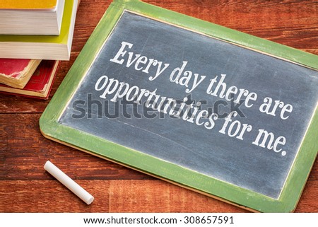 Every day there are opportunities for me - positive affirmation phrase on a slate blackboard with a white chalk and a stack of books against rustic wooden table