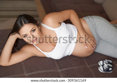 Pregnant woman at home lying on the sofa. Baby shoes.