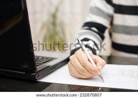 man is writing document or studying with a laptop beside at home