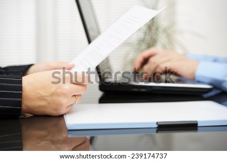 Lawyer is reading contract and business client is typing on laptop